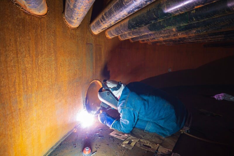welding male worker metal is part machinery plate tank beam pipe construction flash spark inside confined