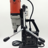 מקדחת מגנטית תעשייתית 1500W Weldon של B.Tech במבט צד — גוף מנוע אדום-אפור בחלק העליון, בסיס מגנטי שחור רחב עם שני מתגי הפעלה נפרדים למנוע ולמגנט, ידית כוכב כפולה בכרום עם אחיזות גומי שחורות להזנה אנכית מדויקת, ומיכל קירור שקוף עם צינור גמיש שחור המוביל נוזל לאזור הקידוח. מיועדת לקידוח עד 32 מ"מ בפלדה, מתאימה למסגריות ולאתרי בנייה. מק"ט 0508967.